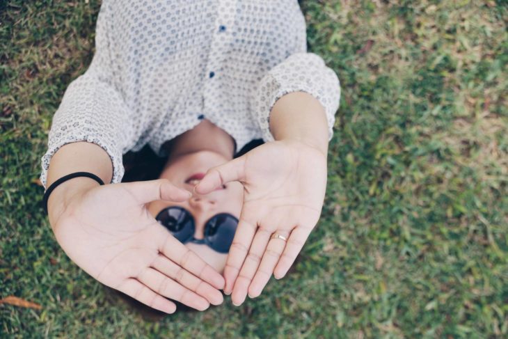Frau liegt im Grass und macht ein Herz